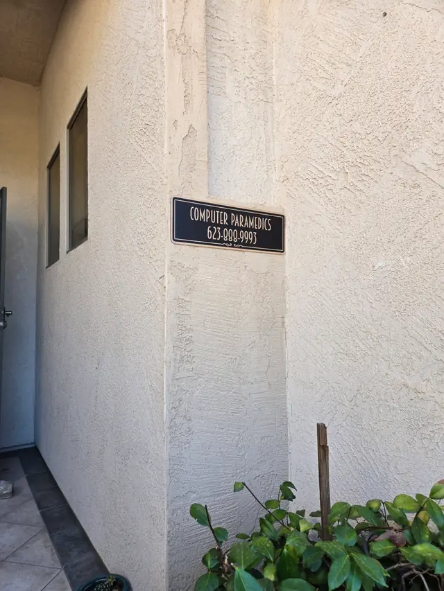 Black wall plaque on a stucco wall reading COMPUTER PARAMEDICS 623-888-9993